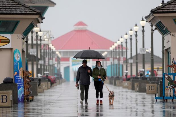 ARCHIVO - Una pareja camina bajo la lluvia con su perro por el muelle de Huntington Beach en Huntington Beach, California, el 6 de febrero de 2024. (Foto AP/Marcio José Sánchez, archivo)